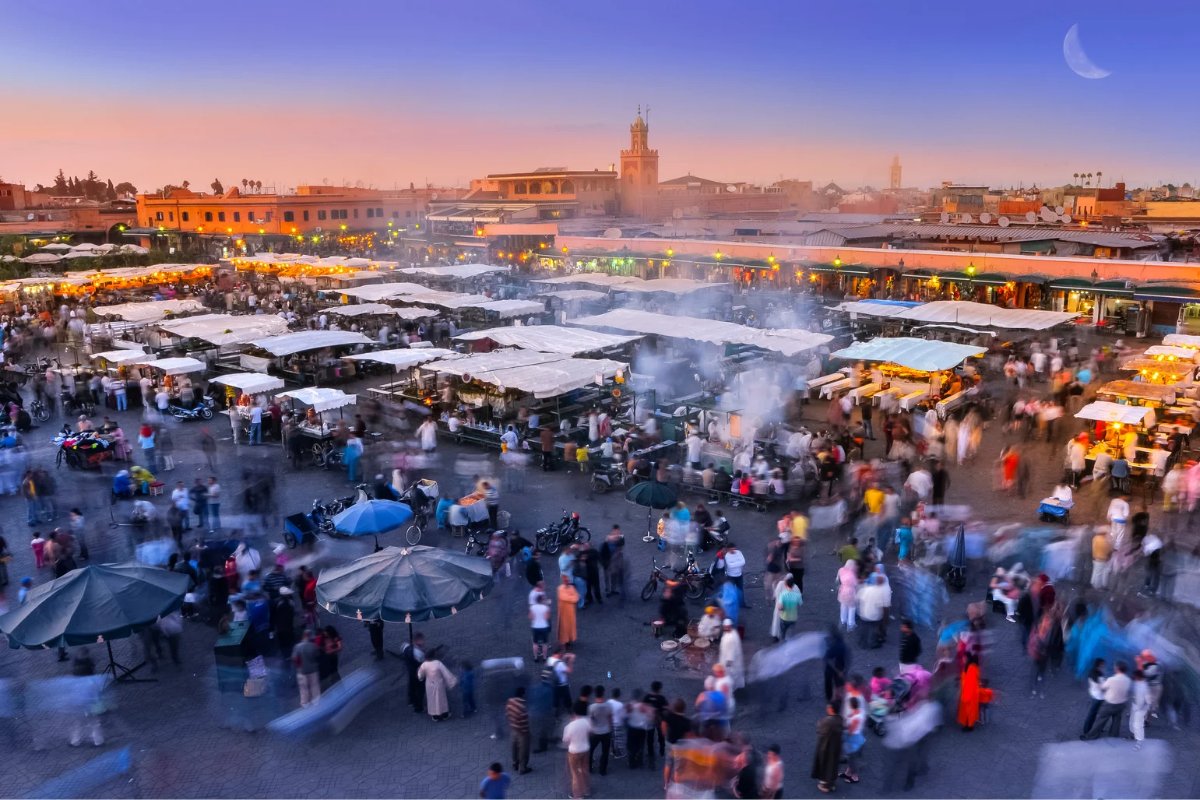 Jemaa el-Fnaa at dusk, Marrakesh — stalls, smoke and the minaret under a crescent moon